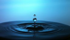 Water drop splashes into water, creating ripples, blue background.