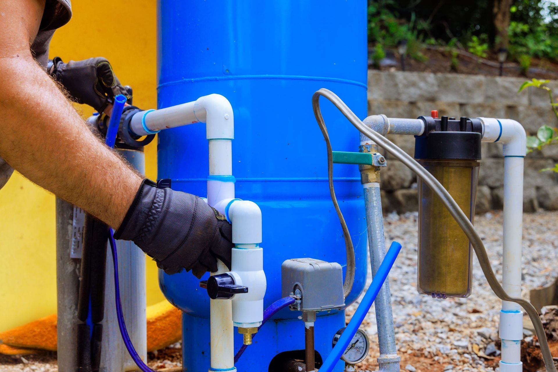 Person in black gloves working on a blue water tank with white pipes.