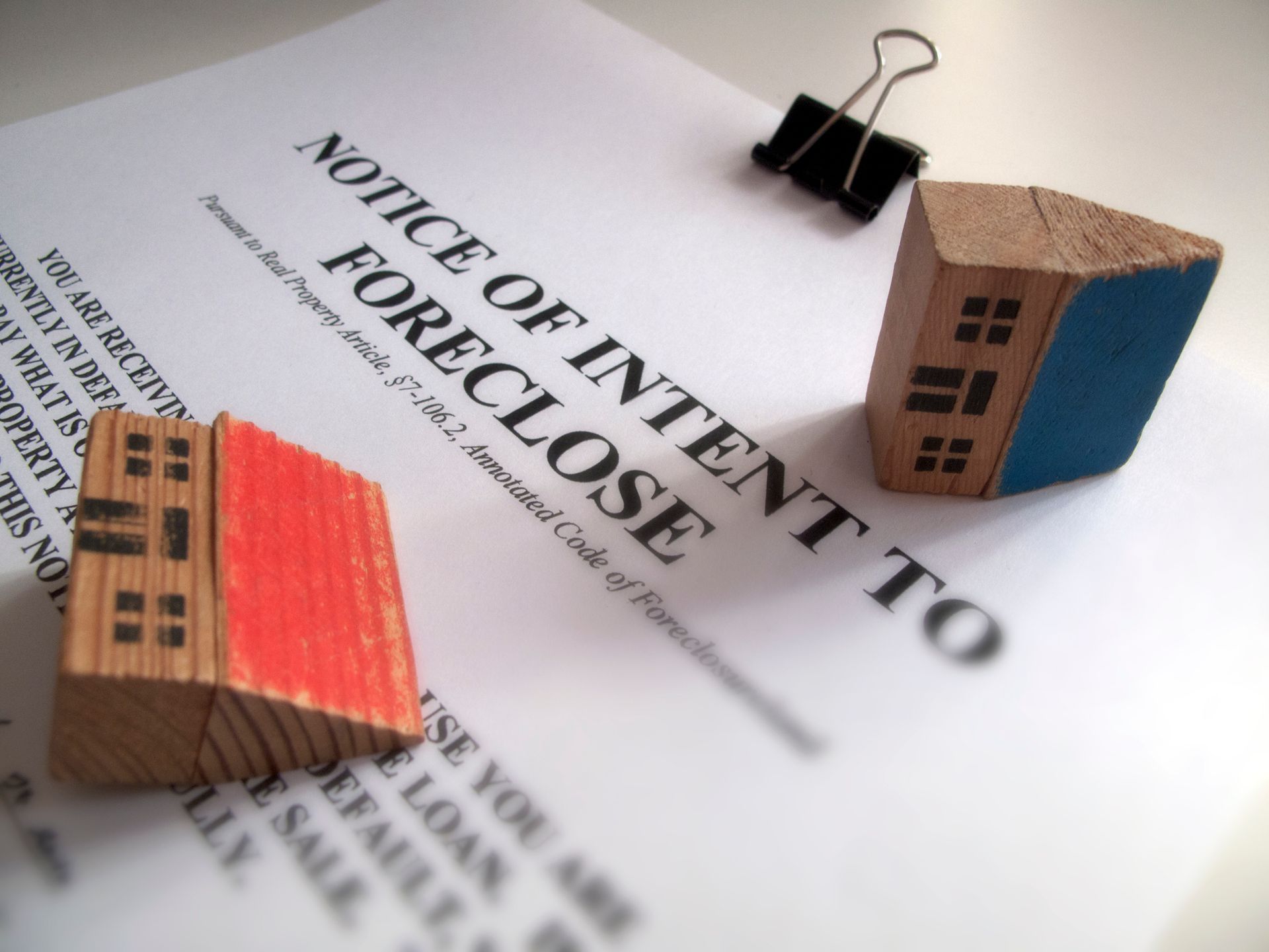 Notice of Intent to Foreclose document with wooden house blocks, held by a binder clip.