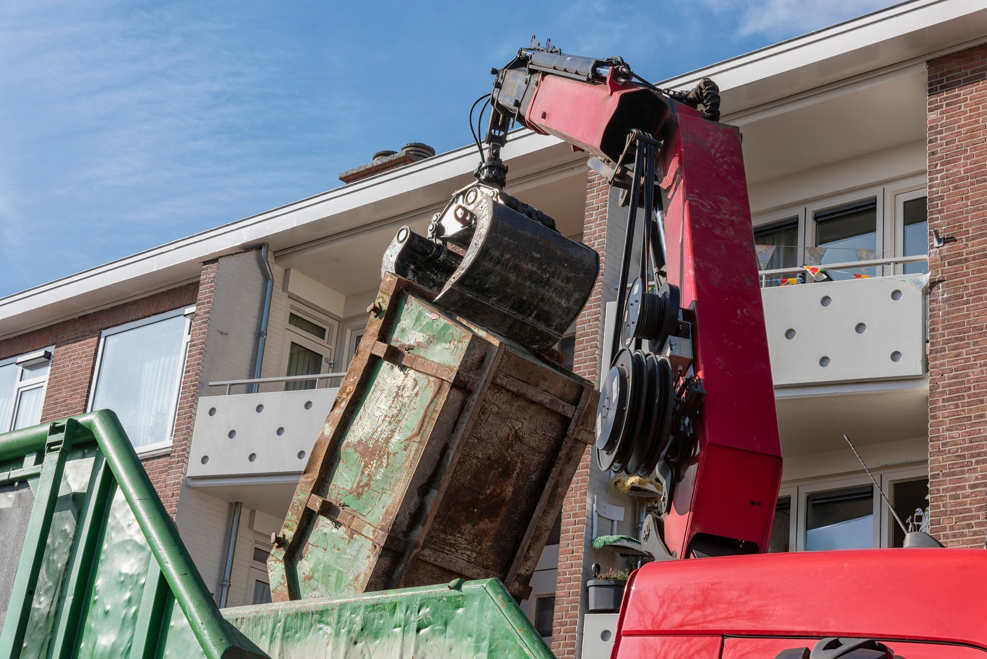 A crane lifting a rusty container from a truck, in front of a white building.