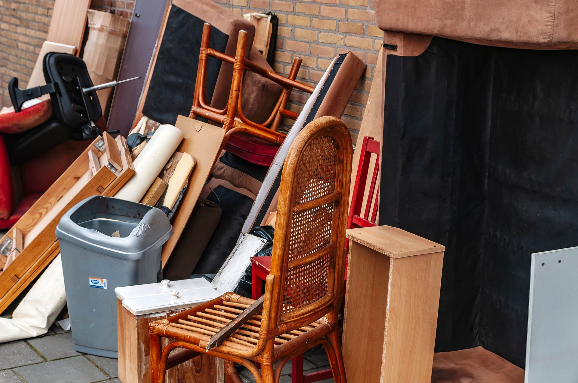 Pile of discarded furniture and trash on a city sidewalk, including chairs, wood planks, and a trash can.