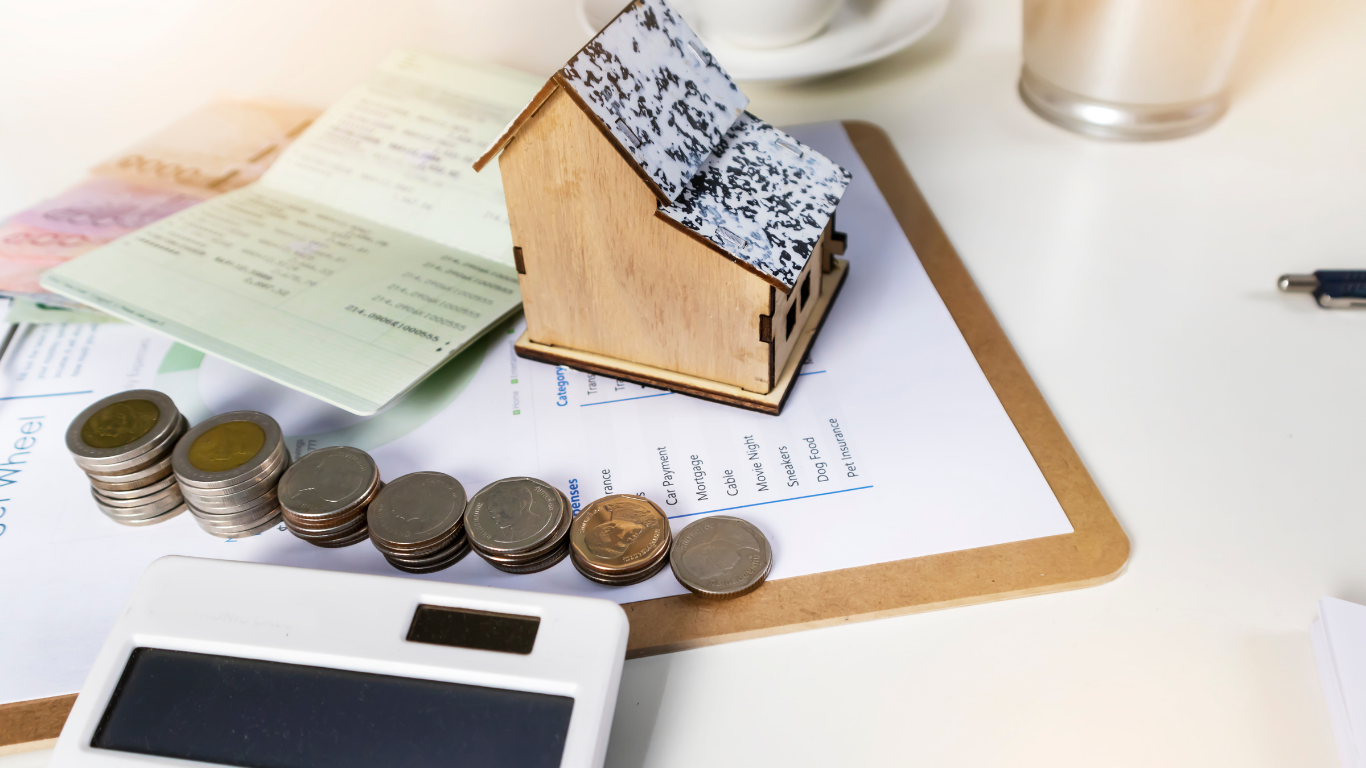 Wooden house model, coins, calculator, and financial documents on a desk, representing home finances.