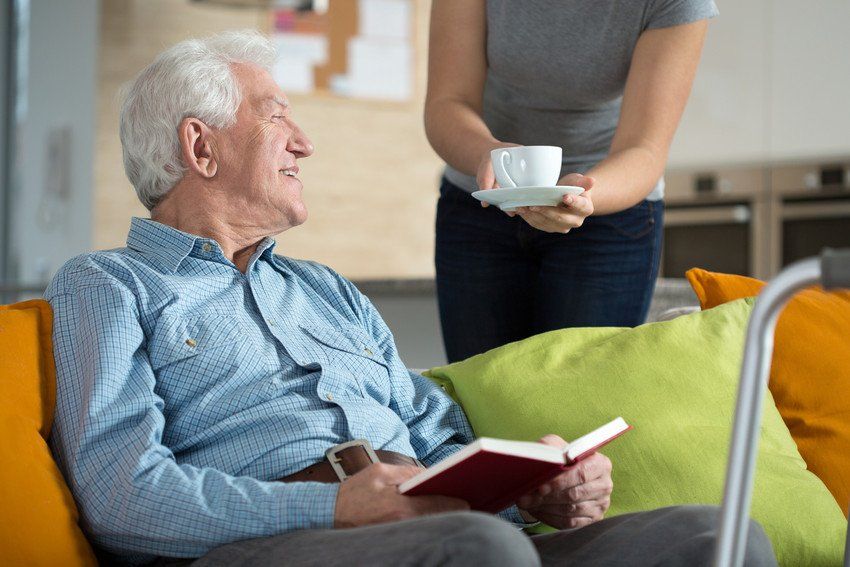 Elderly happy man reading a book and being offered tea