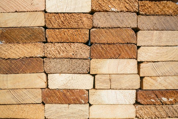 Tablones de madera apilados, en diferentes tonalidades de marrón y tostado, mostrando la veta transversal.