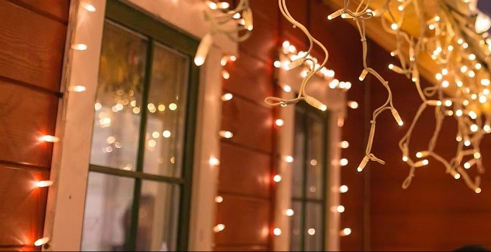 Red house with windows and white trim, decorated with warm, glowing Christmas lights.