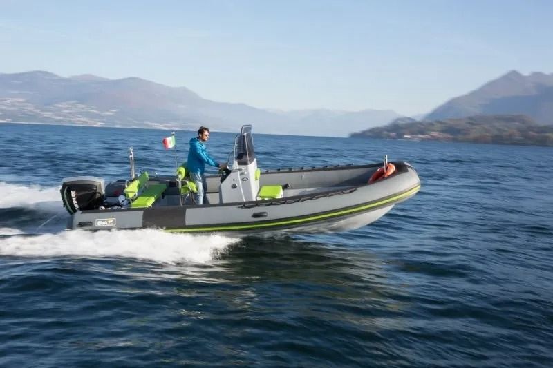 Un gommone che sfreccia su un lago con le montagne sullo sfondo, una persona alla guida.