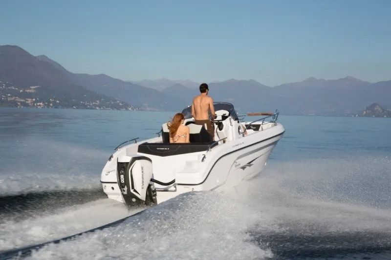 Un motoscafo bianco sfreccia su un lago con due persone a bordo e le montagne sullo sfondo.