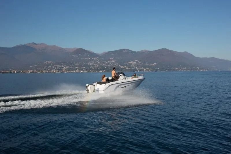 Un motoscafo bianco sfreccia su un lago blu, con le montagne sullo sfondo, due persone a bordo.