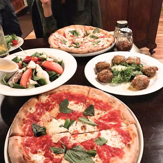 A table topped with pizzas , salads and meatballs.