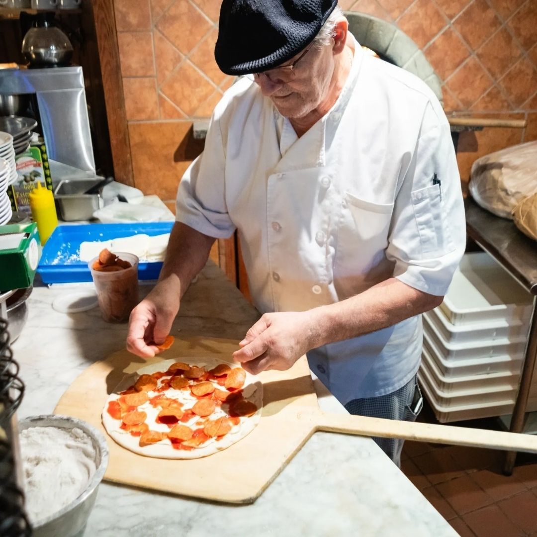 A man is putting tomatoes on a pizza on a wooden paddle