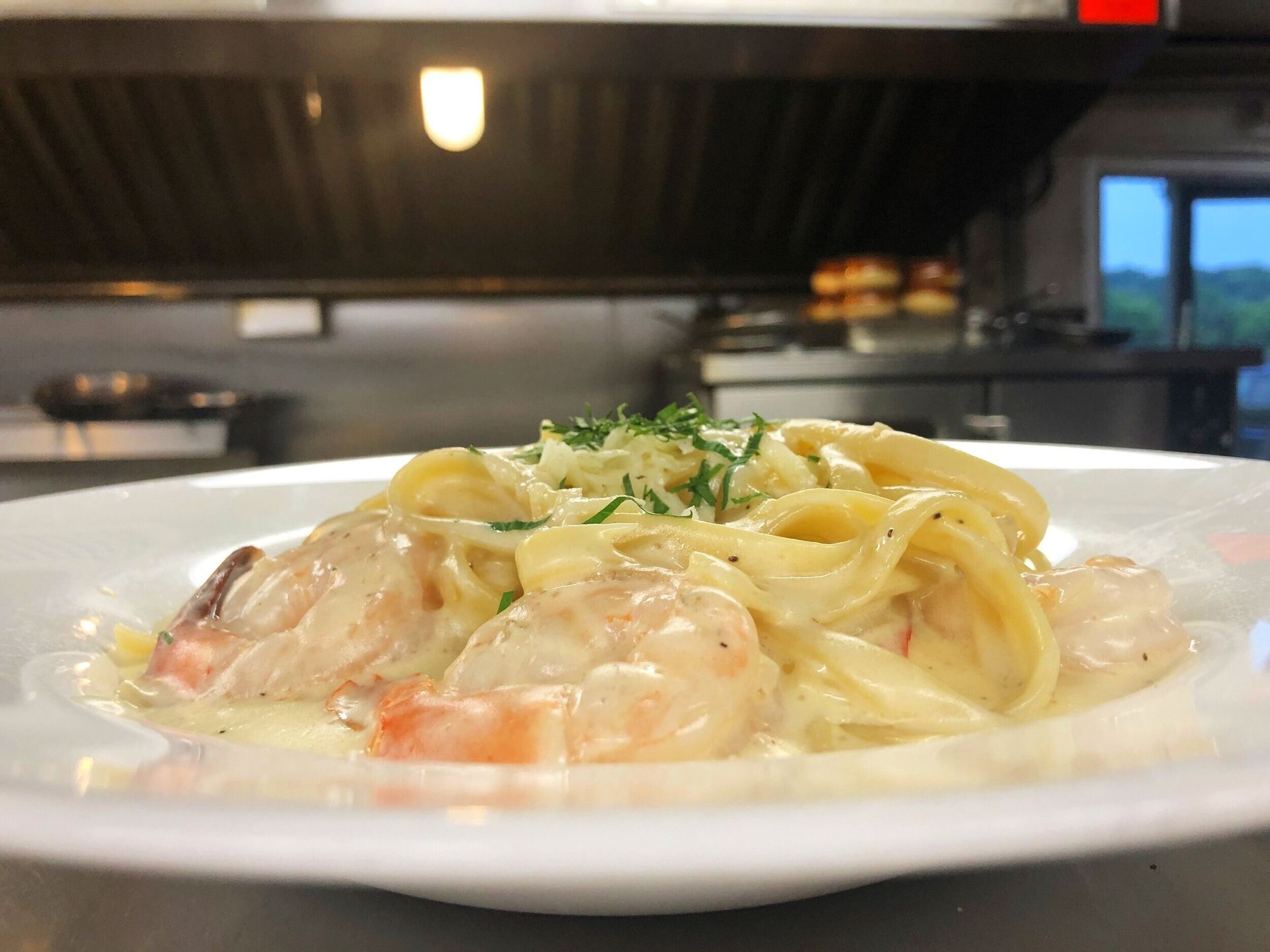 A close up of a plate of pasta with shrimp on a table in a kitchen.