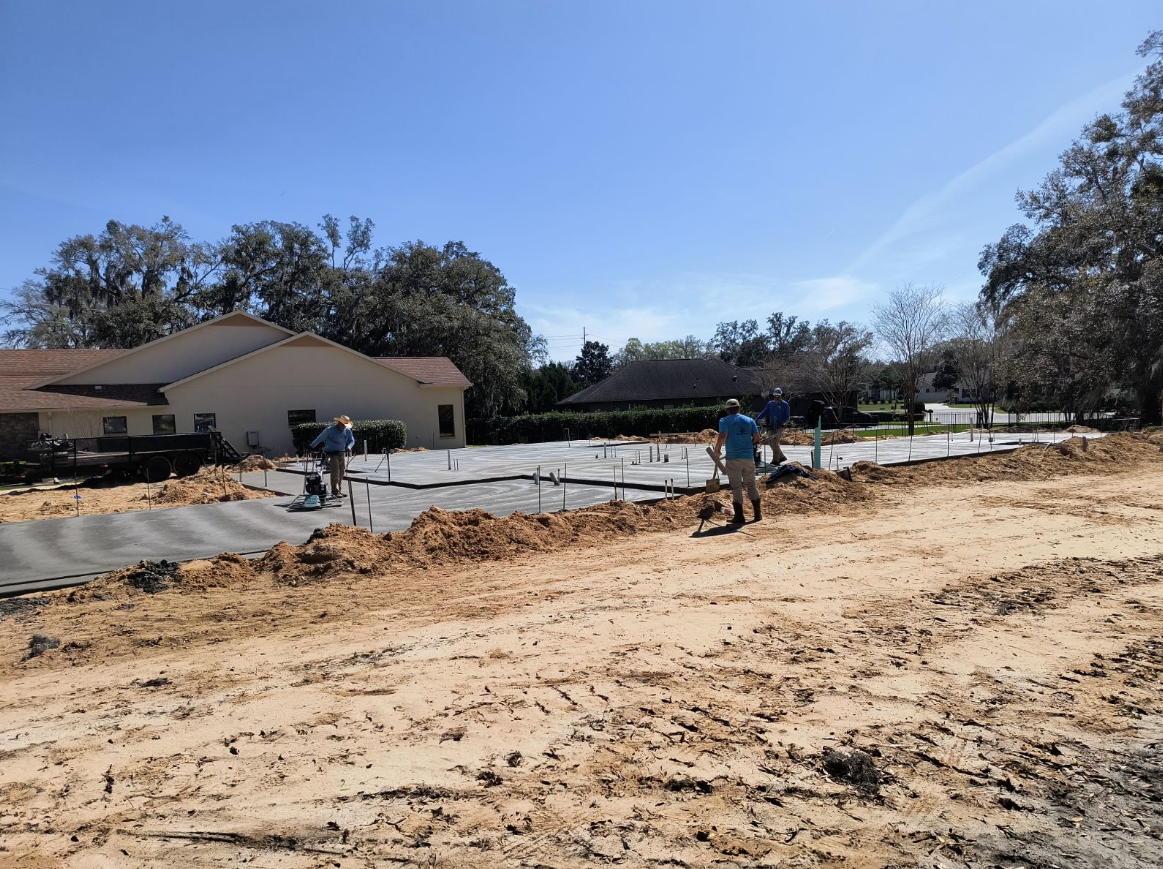 A group of people are standing in a dirt field in front of a house.