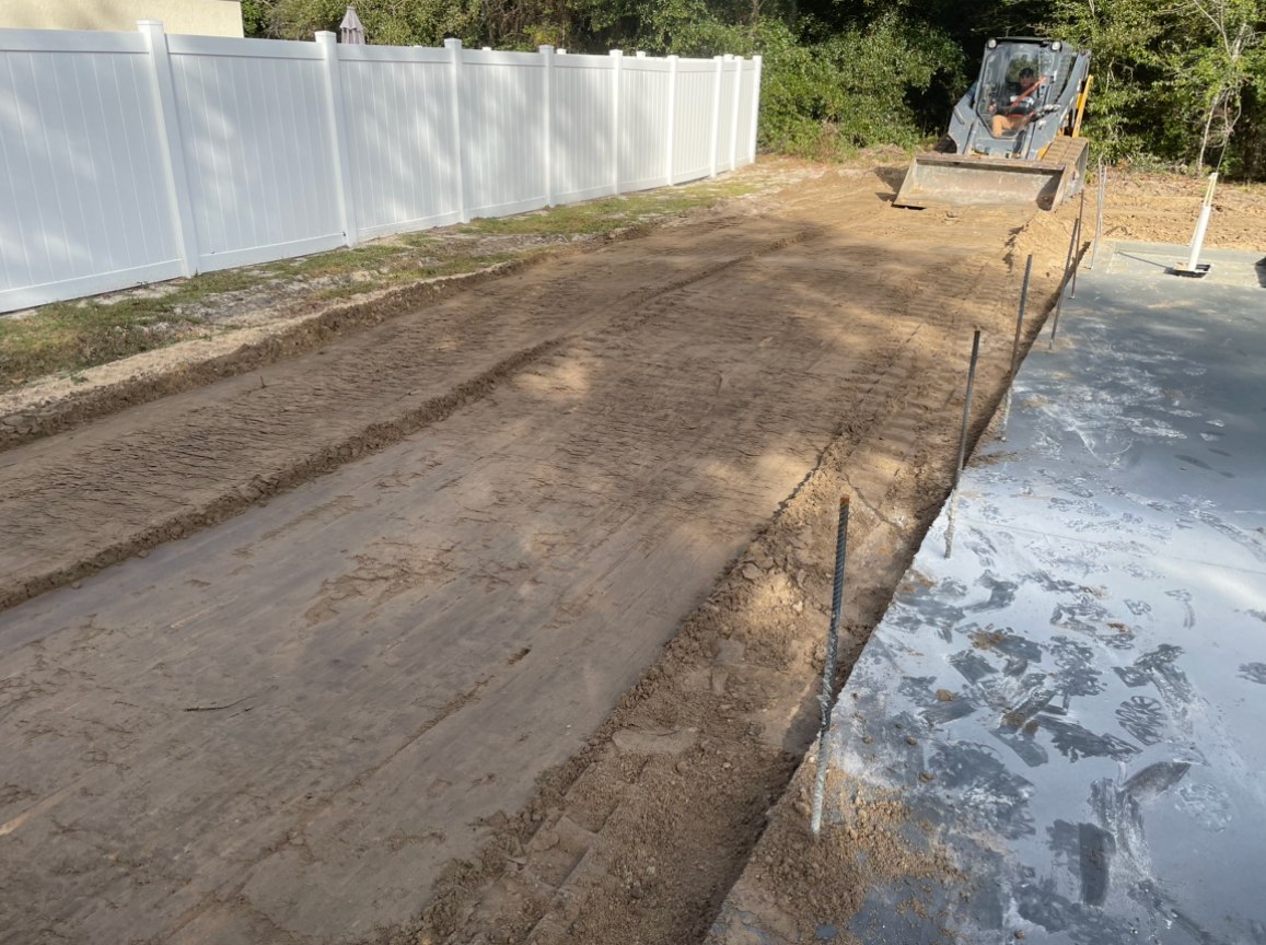 A bulldozer is working on a dirt road next to a white fence.