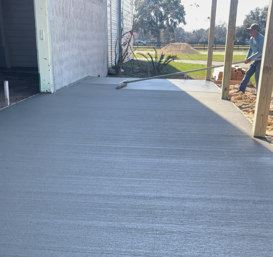 A man is standing on a concrete porch with a broom.