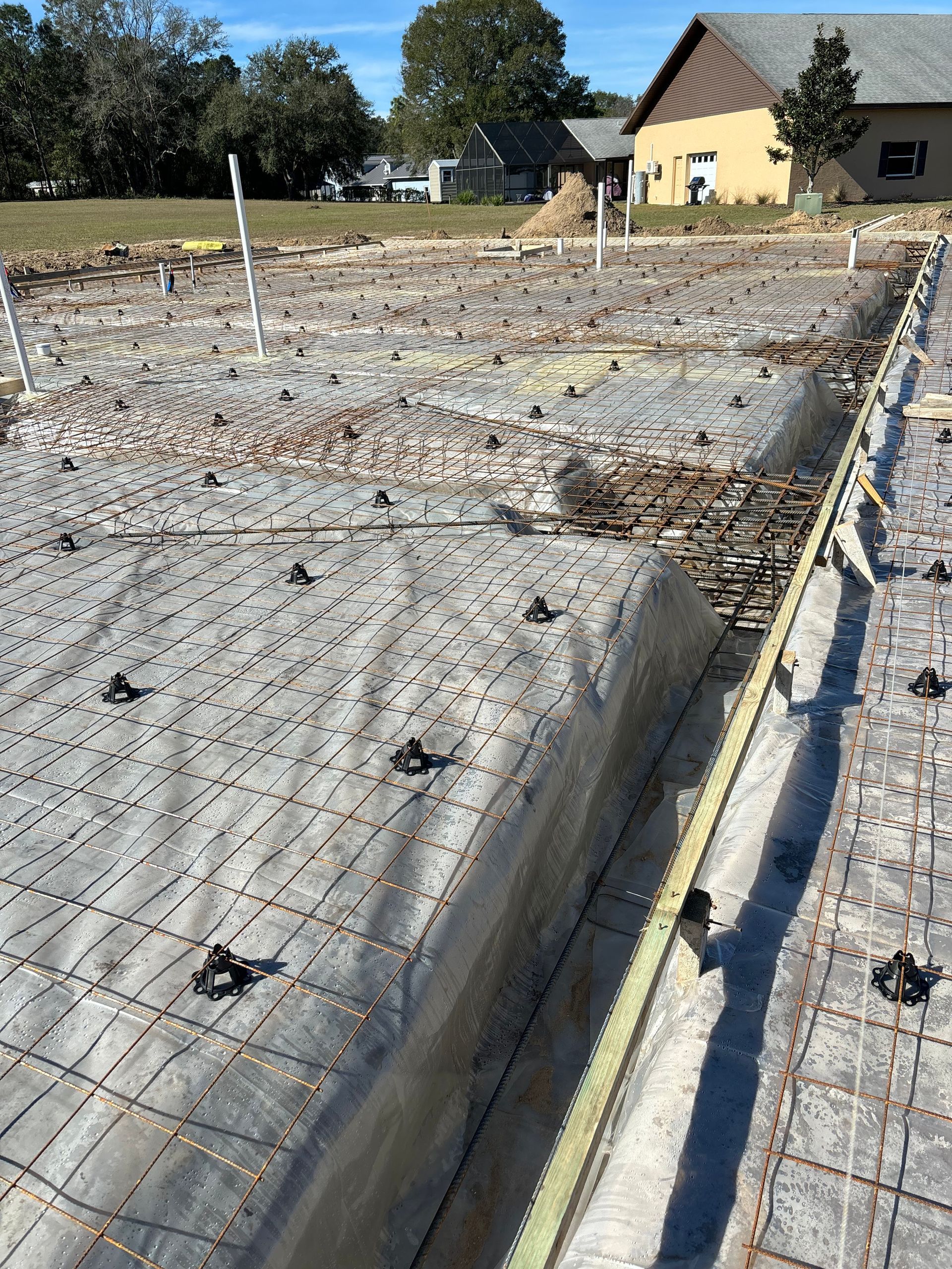 A concrete foundation is being built in a field with a house in the background.