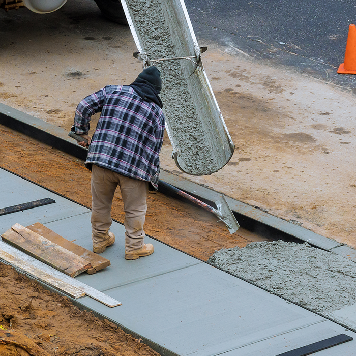 A man in a plaid shirt is pouring concrete on a sidewalk