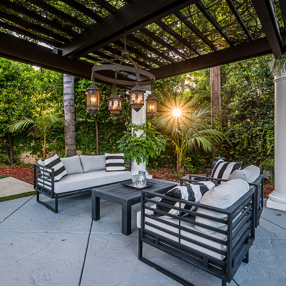 A stamped concrete patio with a couch and chairs under a pergola