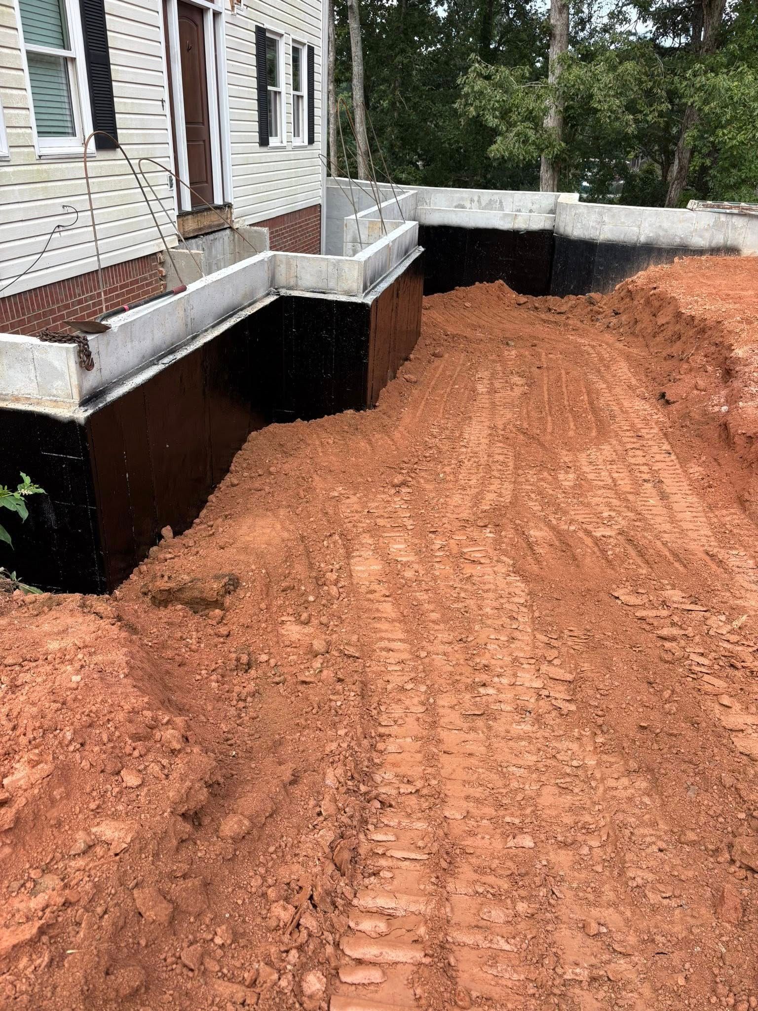 House foundation with black waterproofing and fresh red dirt grading around the base
