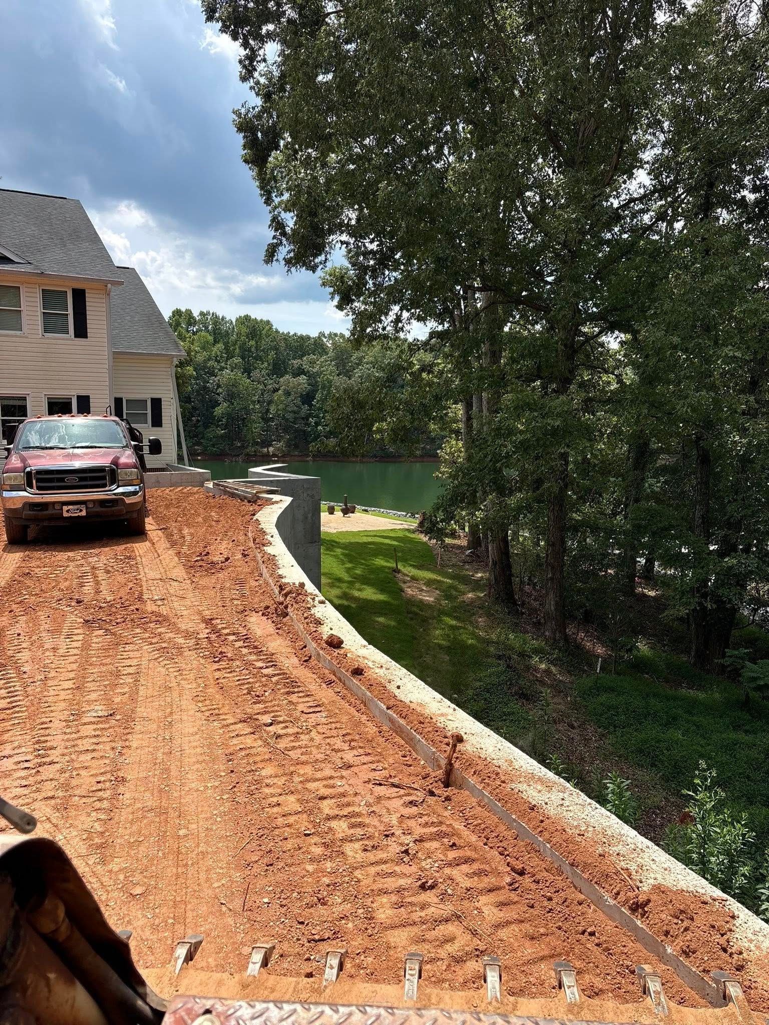 Red clay driveway beside a house, with an SUV parked and a lake visible through trees.