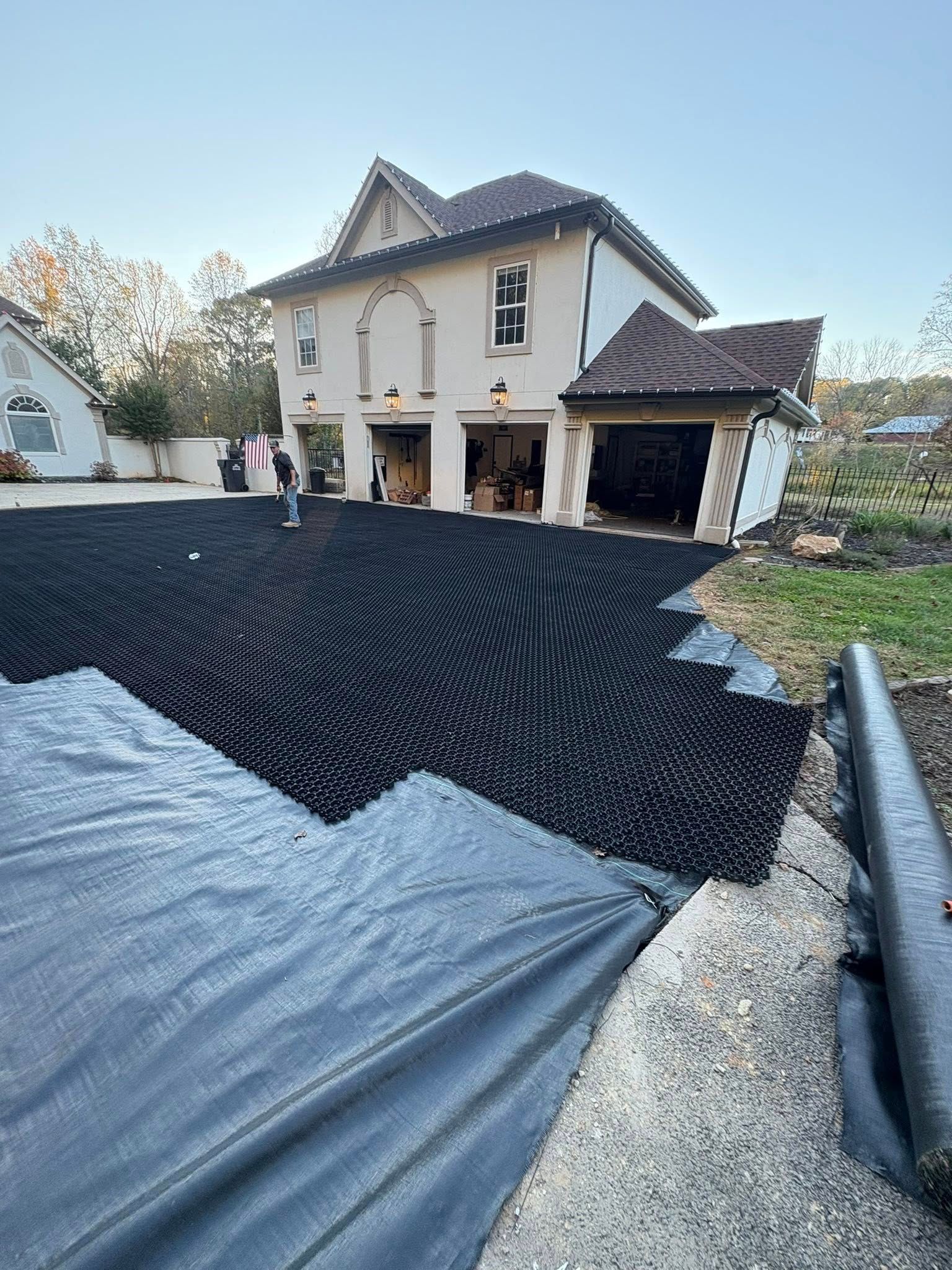 New home driveway under construction, with black gravel, gravel piles, and a two-story house in the background
