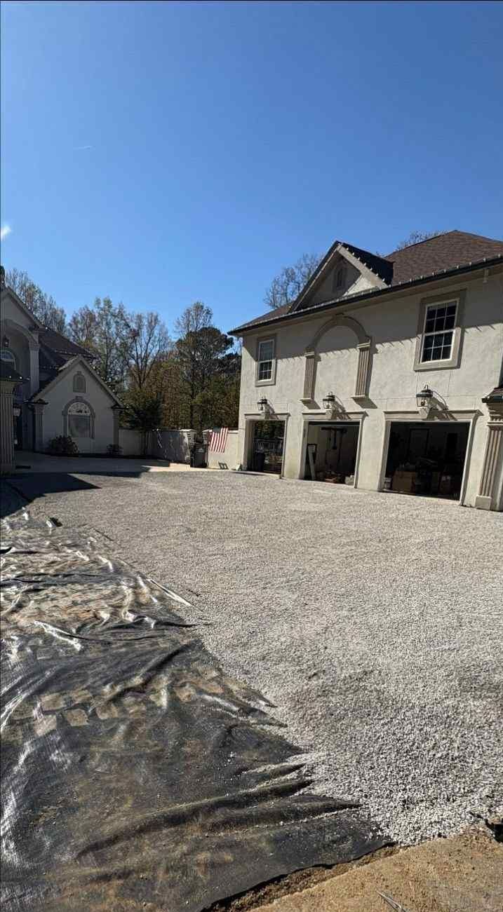 Gravel courtyard beside white buildings under a clear blue sky, with a tarps-covered pile in the foreground