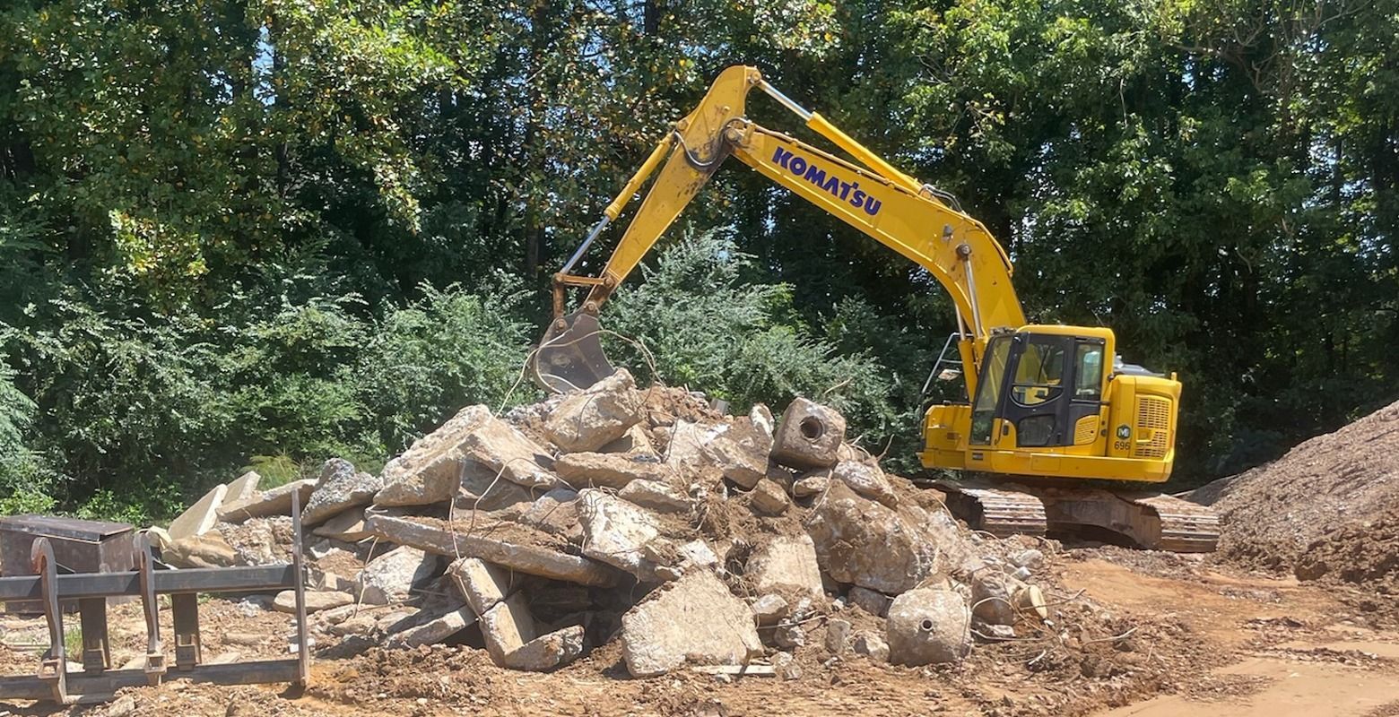 Yellow excavator demolishing a pile of rubble at a construction site
