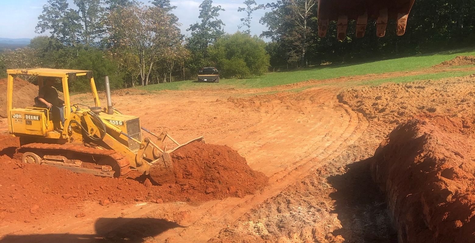 Yellow bulldozer grading red dirt on a construction site with trees and a building in the background