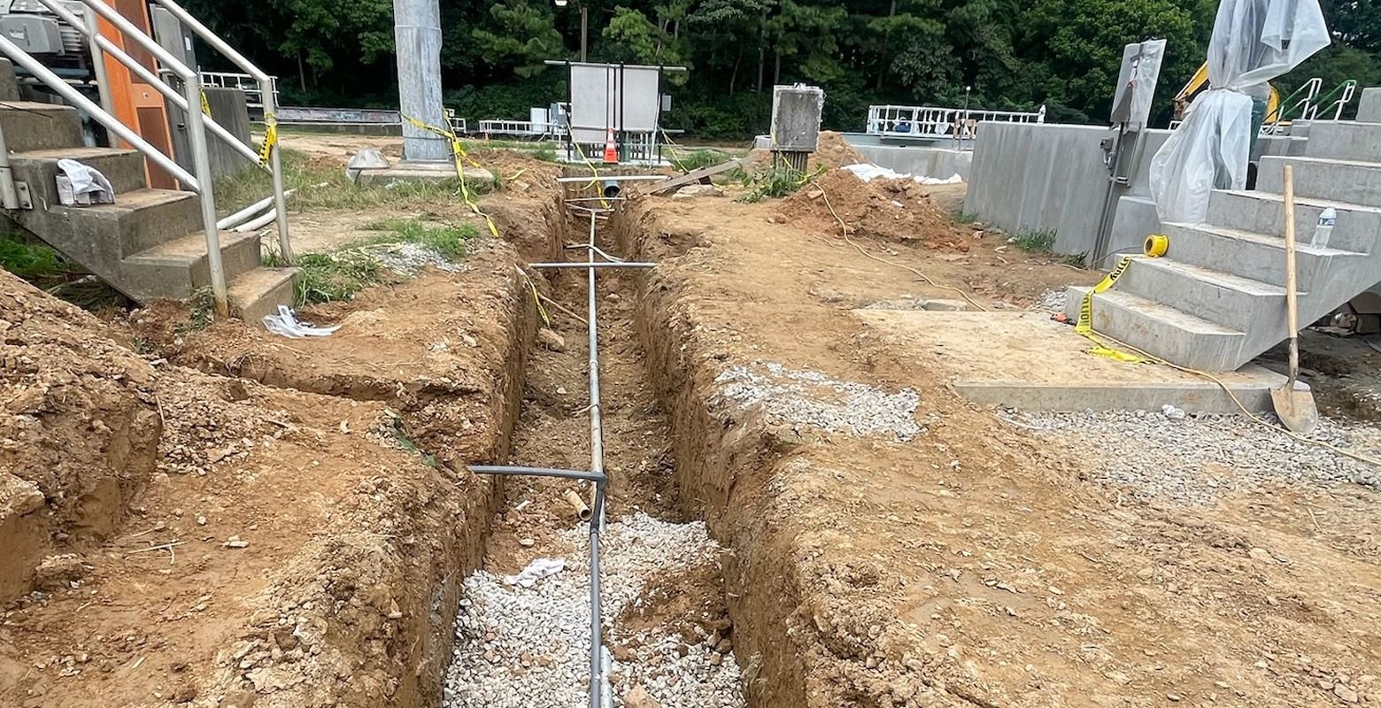 Trenched utility line under construction with exposed pipes and gravel between concrete stairs.