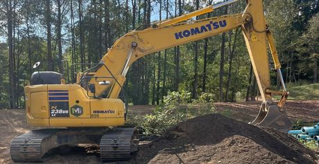Yellow Komatsu excavator digging a dirt pile in a wooded construction site