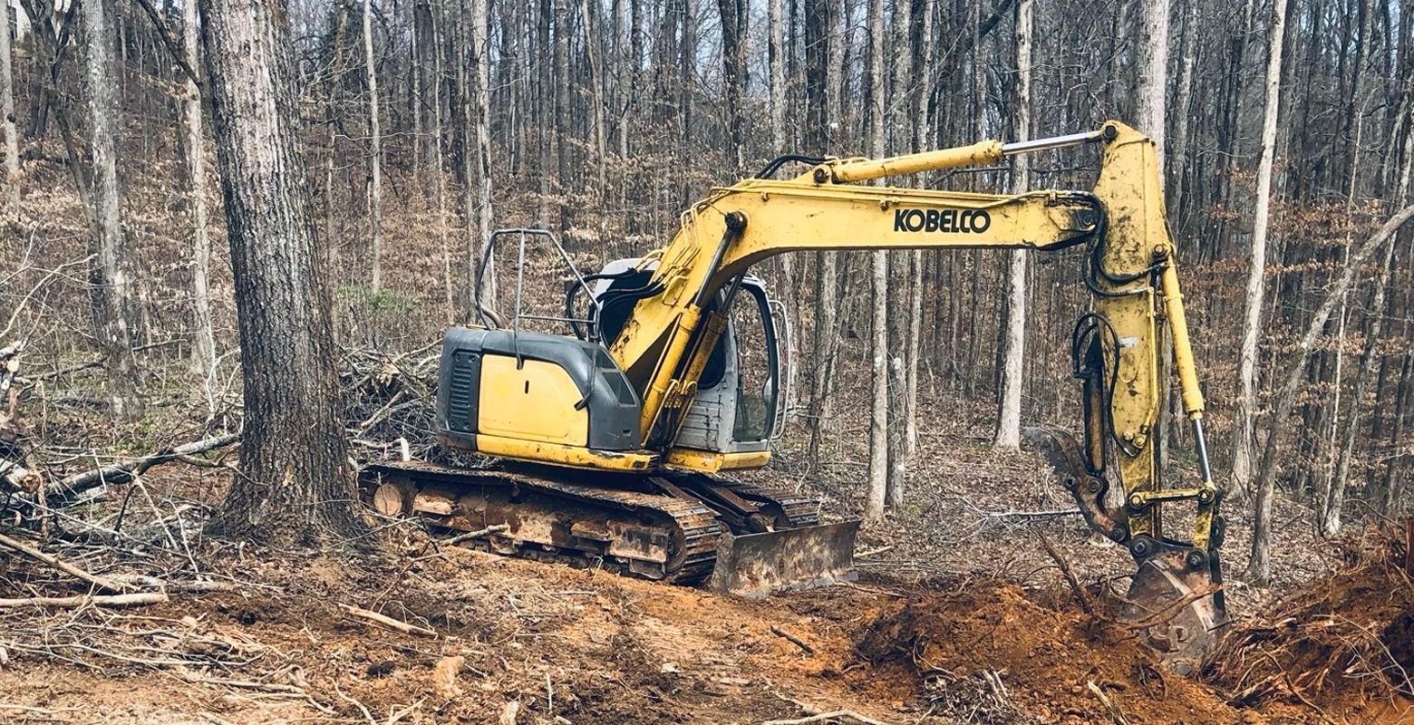 Yellow excavator working in a muddy forest clearing with bare trees