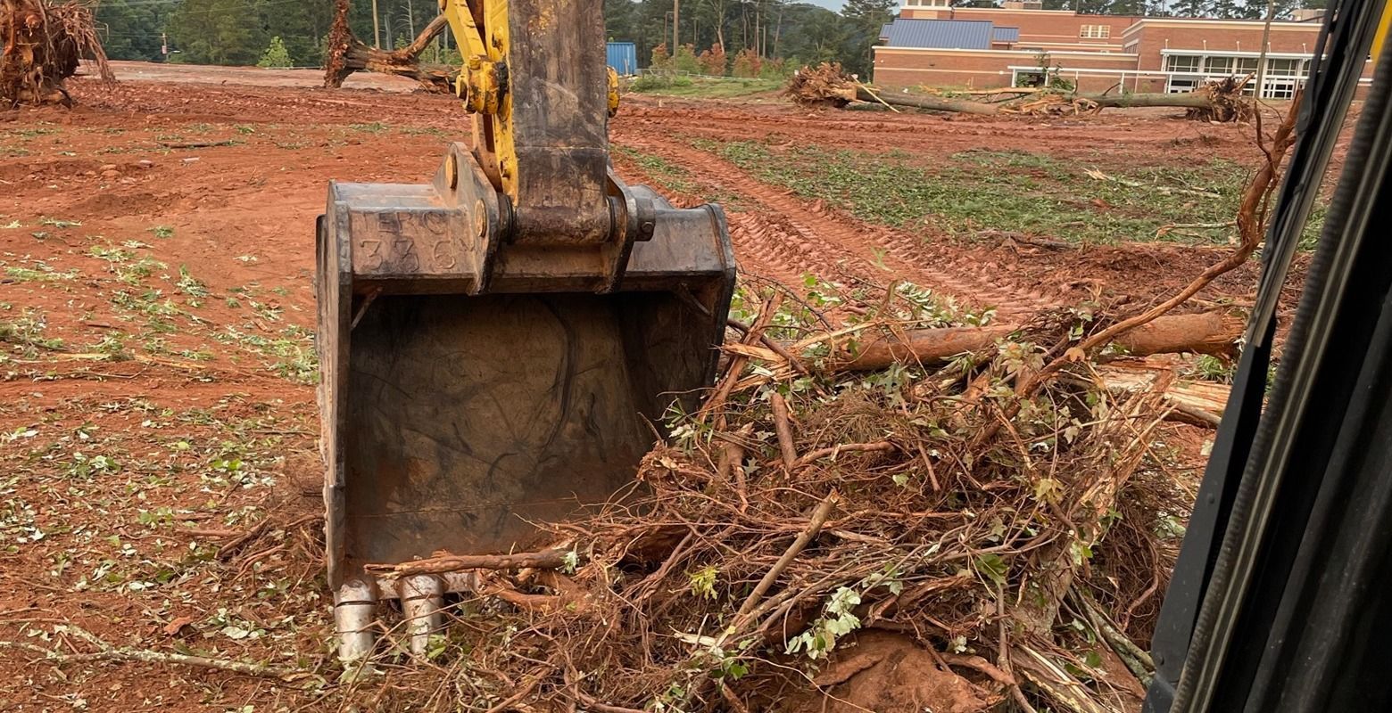 Excavator bucket clearing brush on a red dirt construction site