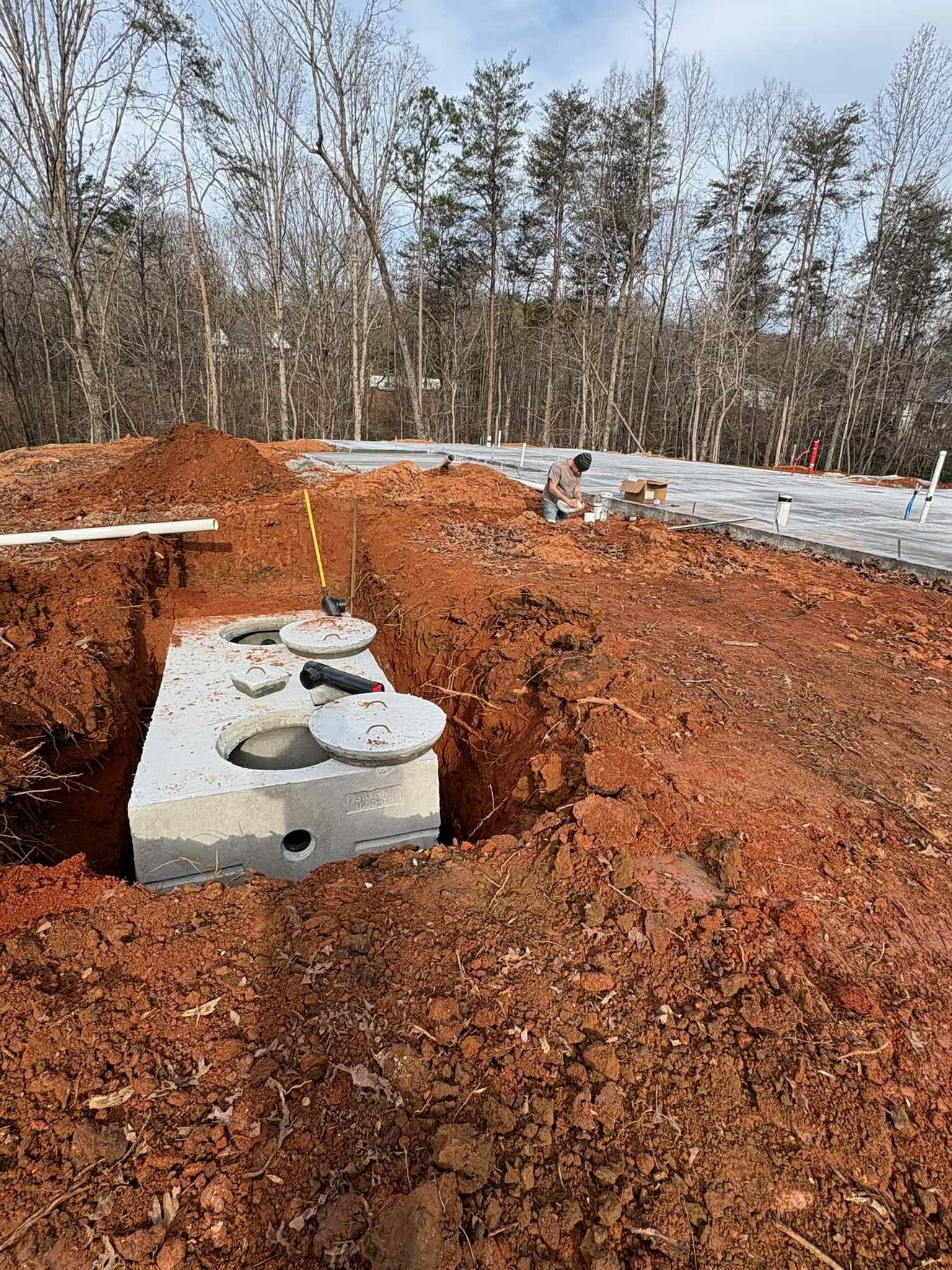 Concrete tank in a dug red-earth excavation, surrounded by trees and plastic sheeting.