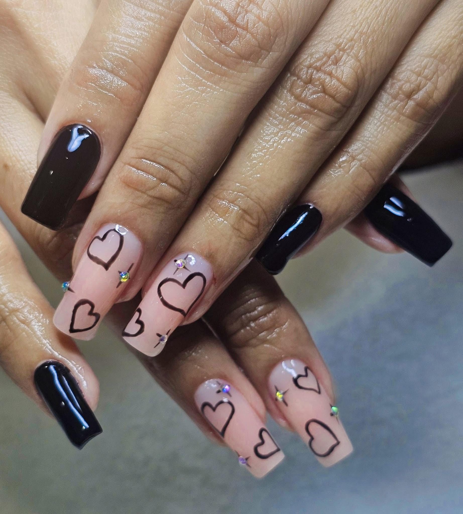 Hand with long square nails: black and pink with heart designs and rhinestones.