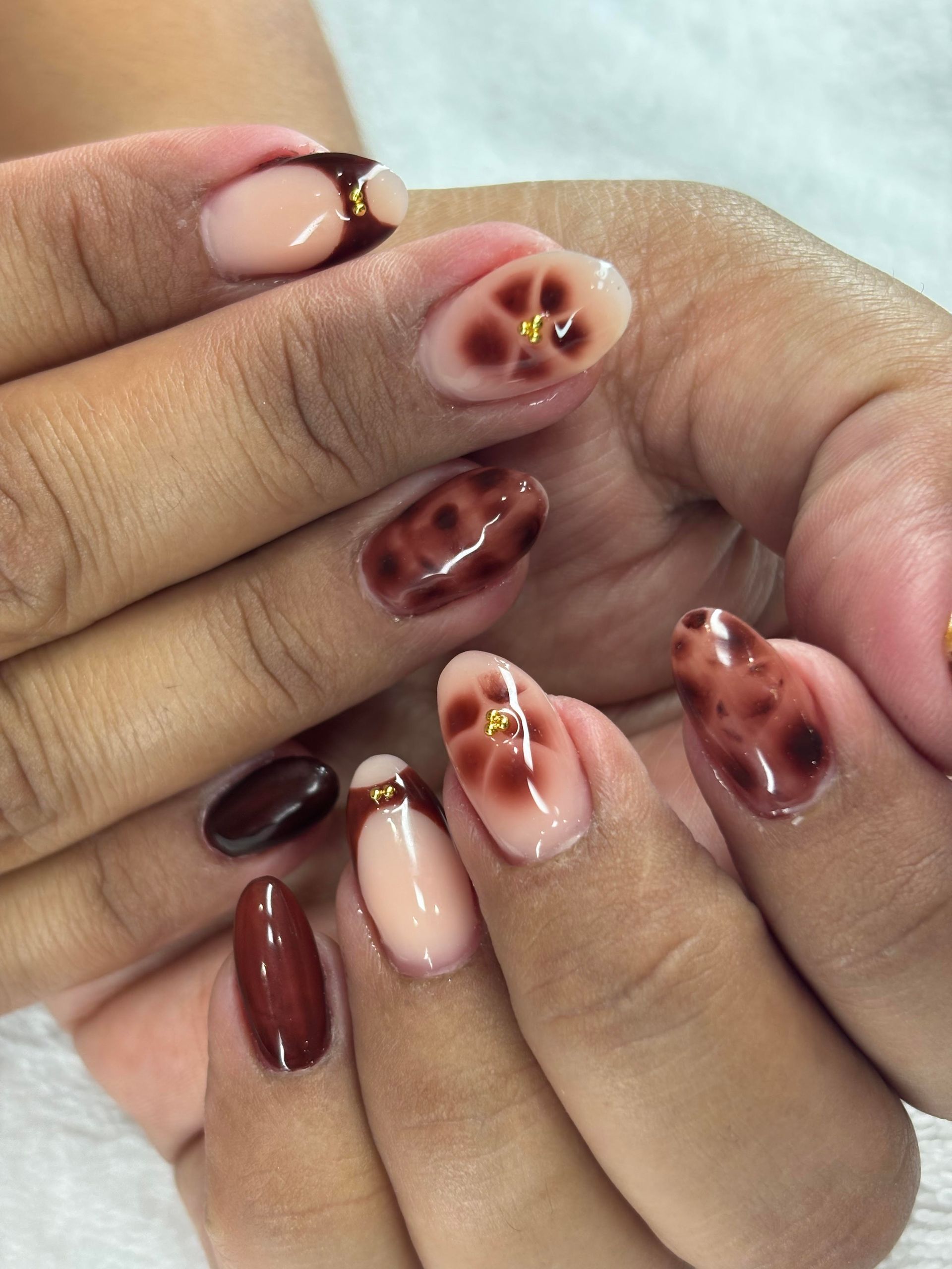 Manicured nails in nude, brown and floral designs, with gold accents.