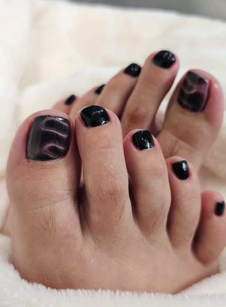 Feet with black nail polish, big toes decorated with swirling black and red designs.