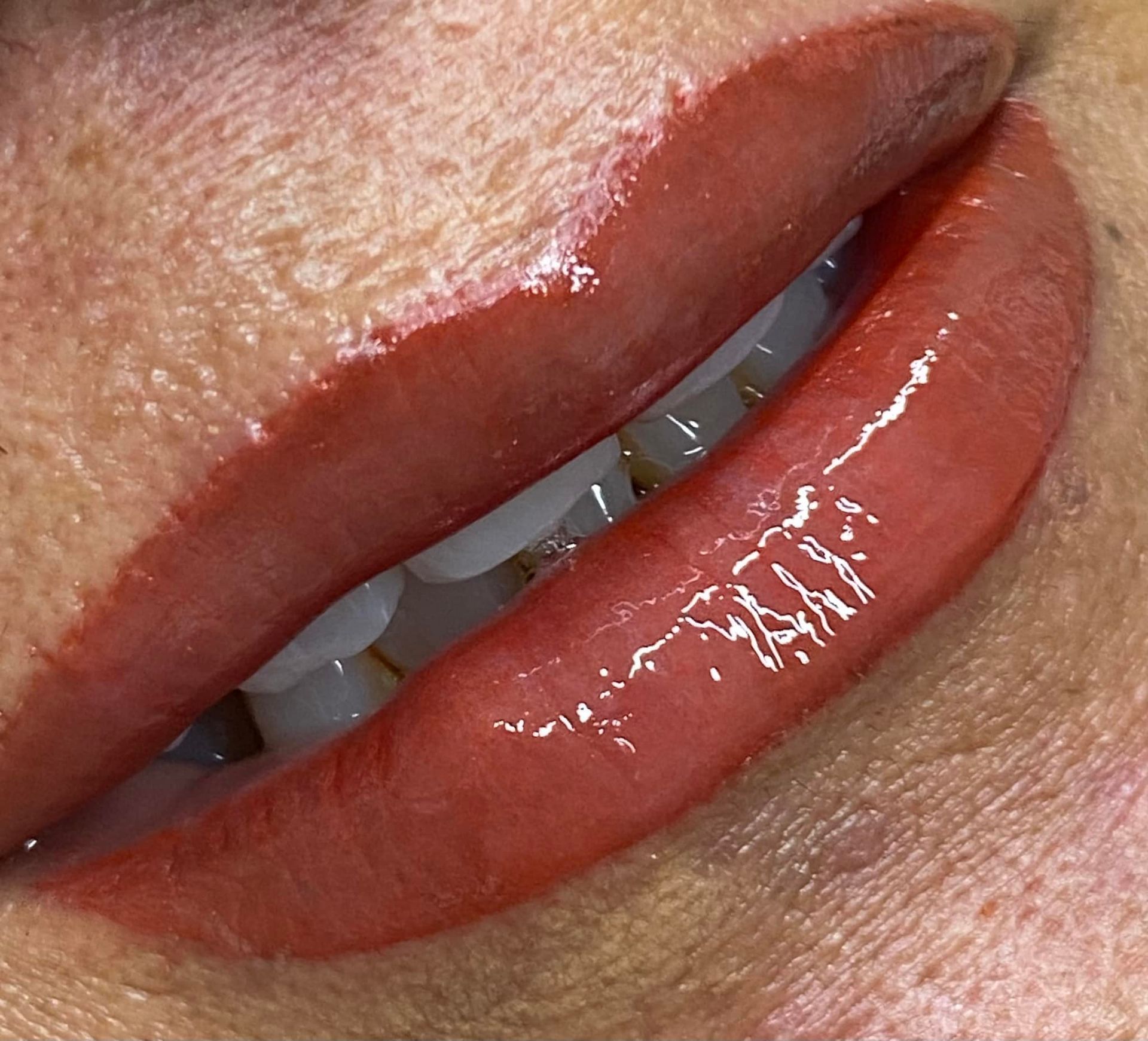 Close-up of a person's lips, lightly filled with a reddish pigment and glossy lip gloss.