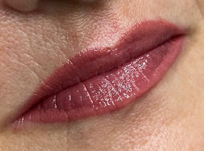 Close-up of a person's lips, painted with a glossy, rose-toned lipstick. The lips are slightly parted.