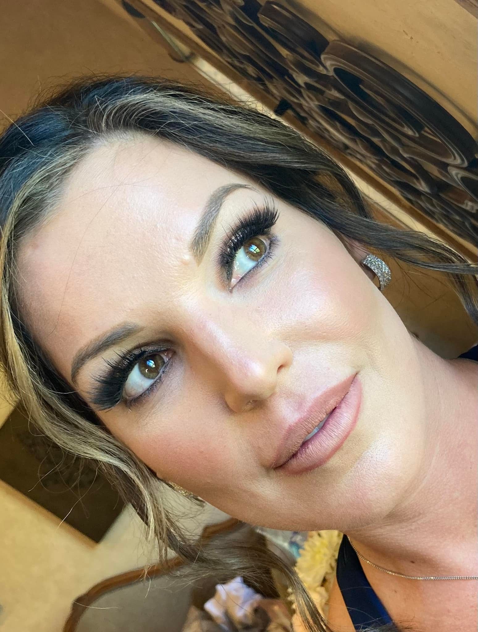 Woman with dark hair, full makeup, and neutral lipstick looking slightly to the side.