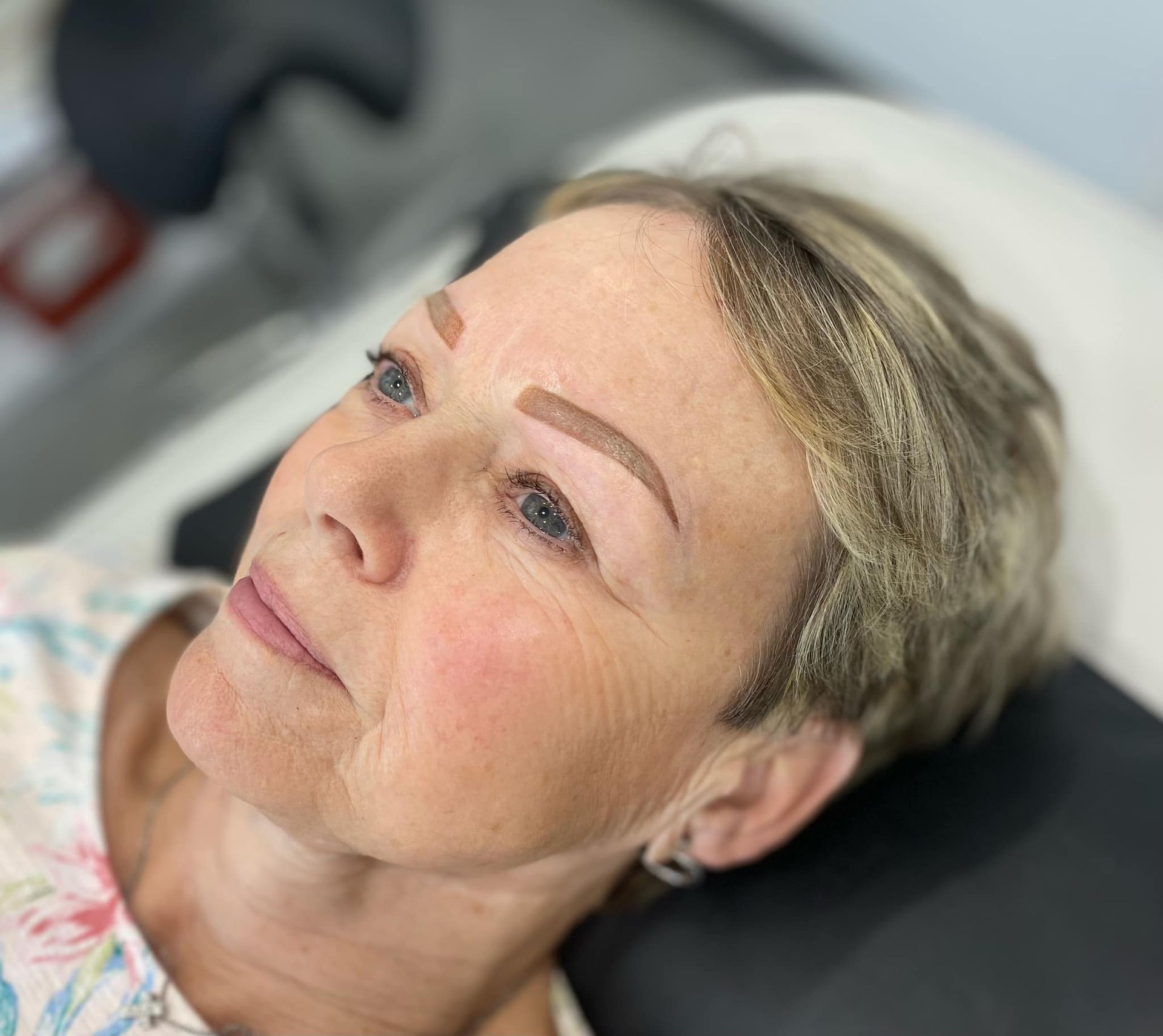 Woman with newly tattooed eyebrows, looking upwards; in a salon setting.