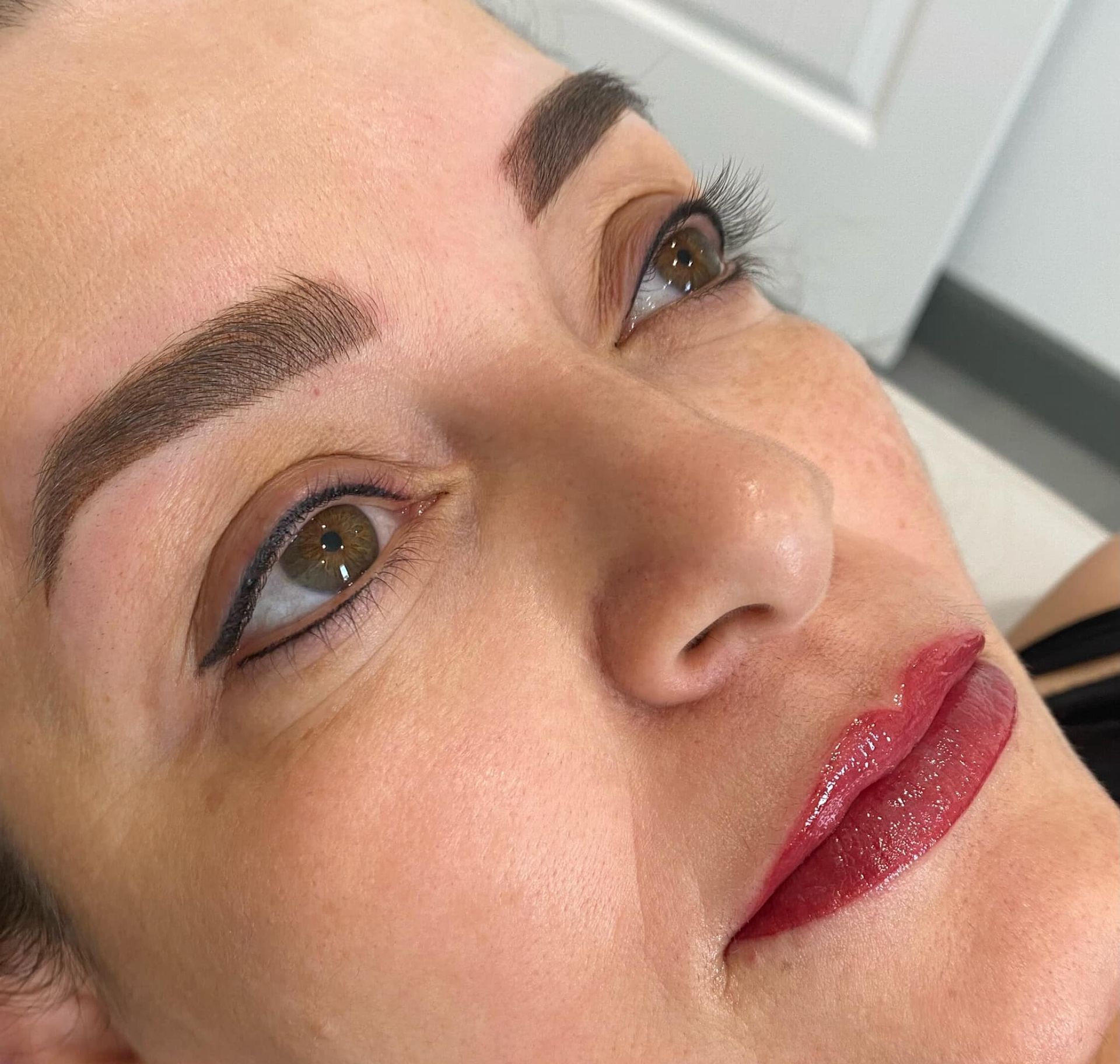 Woman with permanent makeup on eyebrows, eyeliner, and lips. Brown hues and shiny lip color.