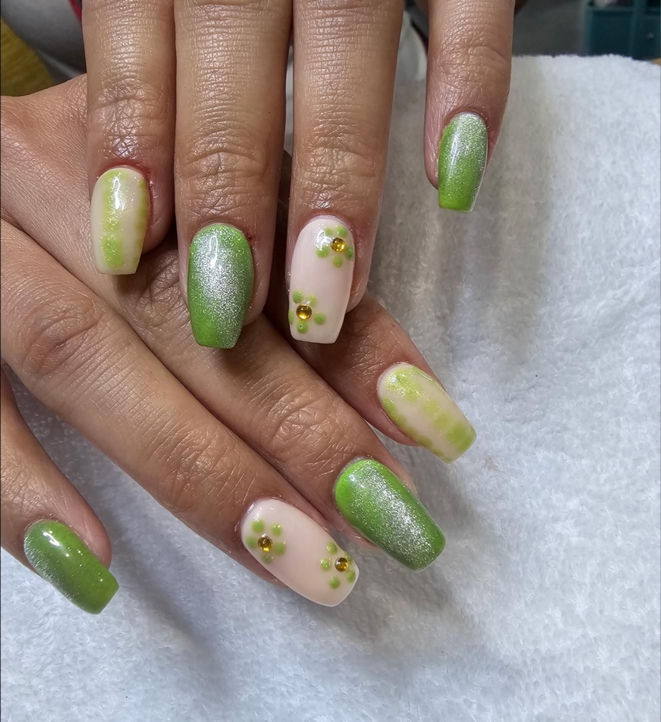 Hands with green and pink coffin-shaped nails, some glittered and adorned with gold flower accents.