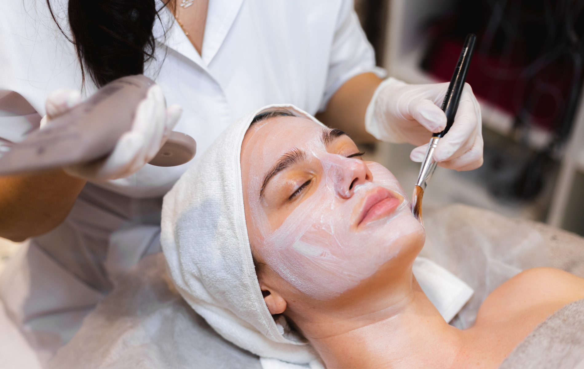 Woman receiving a facial at a spa. A beautician applies a mask to her face with a brush.