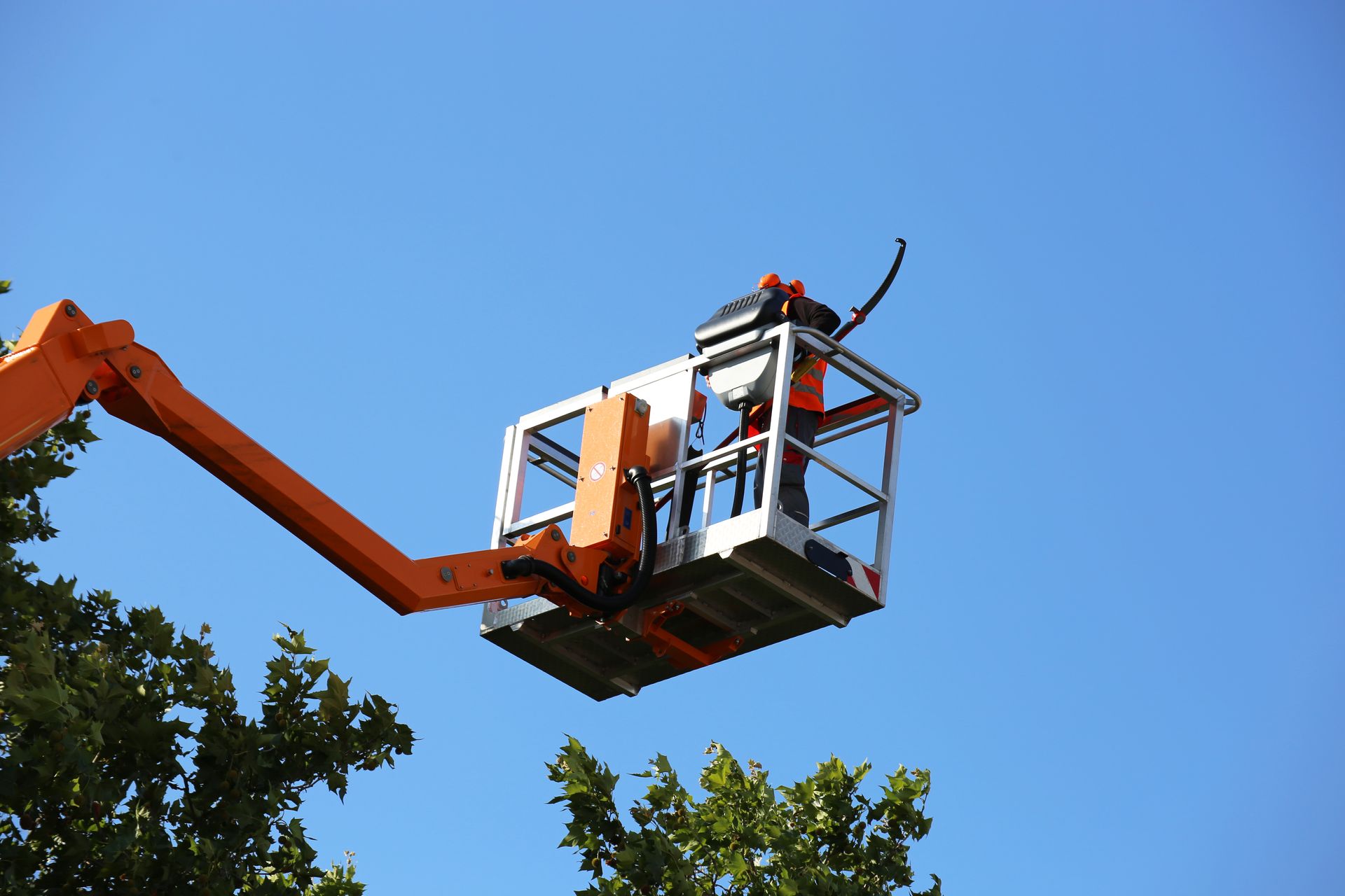 A man is sitting in a bucket on a crane against a blue sky.