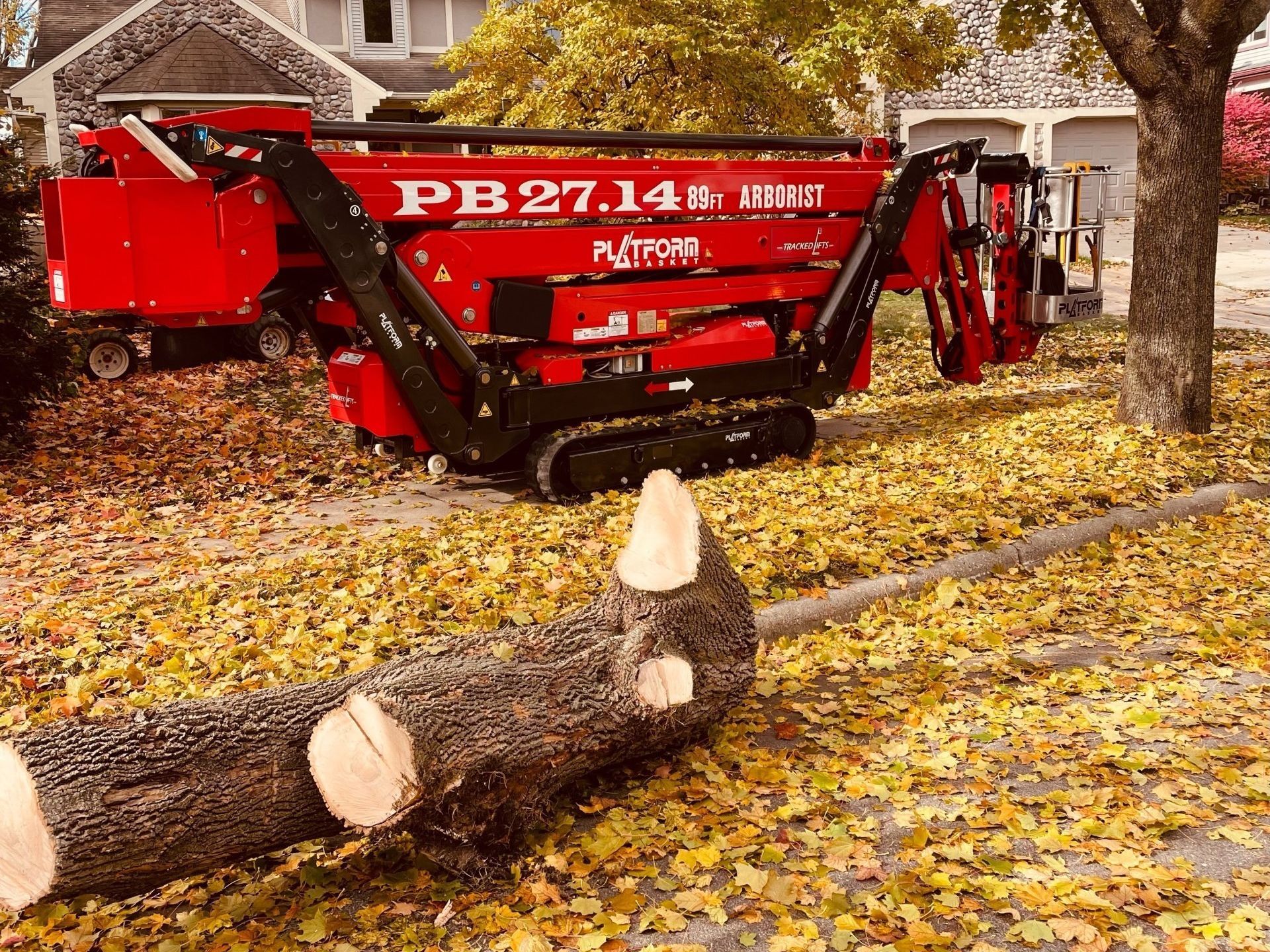 A red machine is cutting down a tree in a yard.