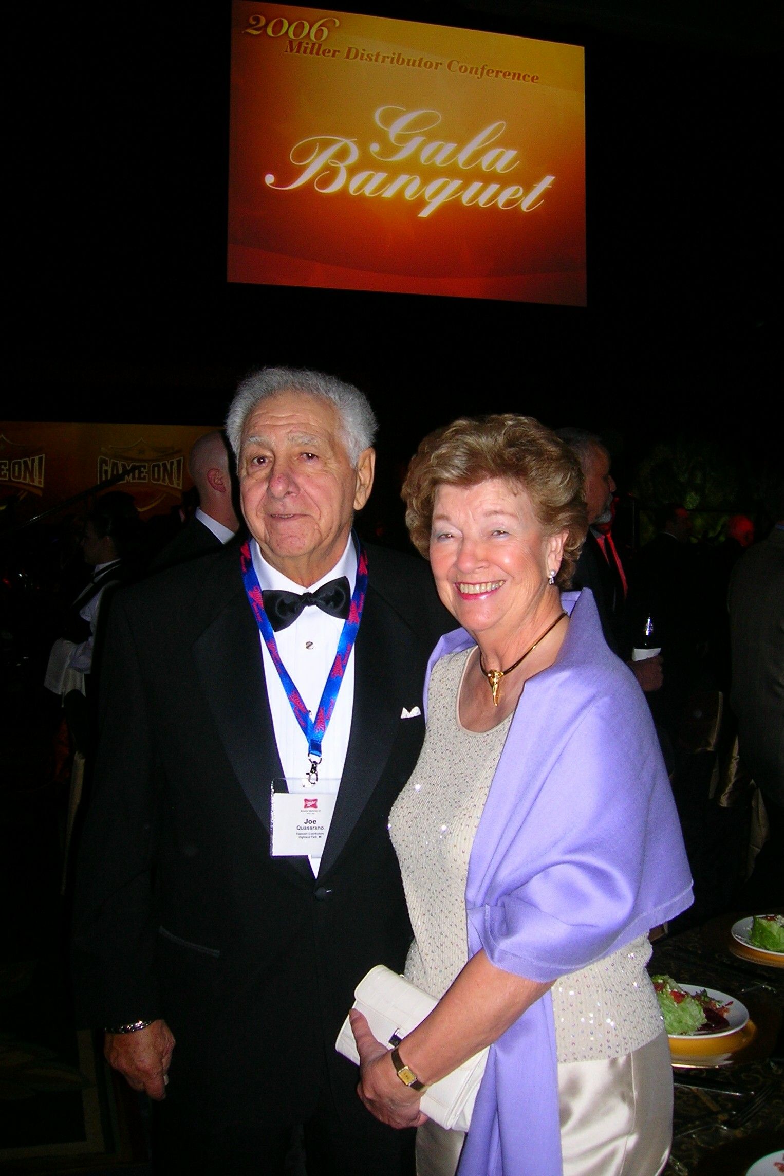 A man and woman are posing for a picture in front of a gala banquet screen