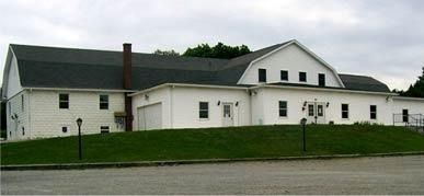 White building with a dark roof, set on a grassy hill. Cloudy sky.