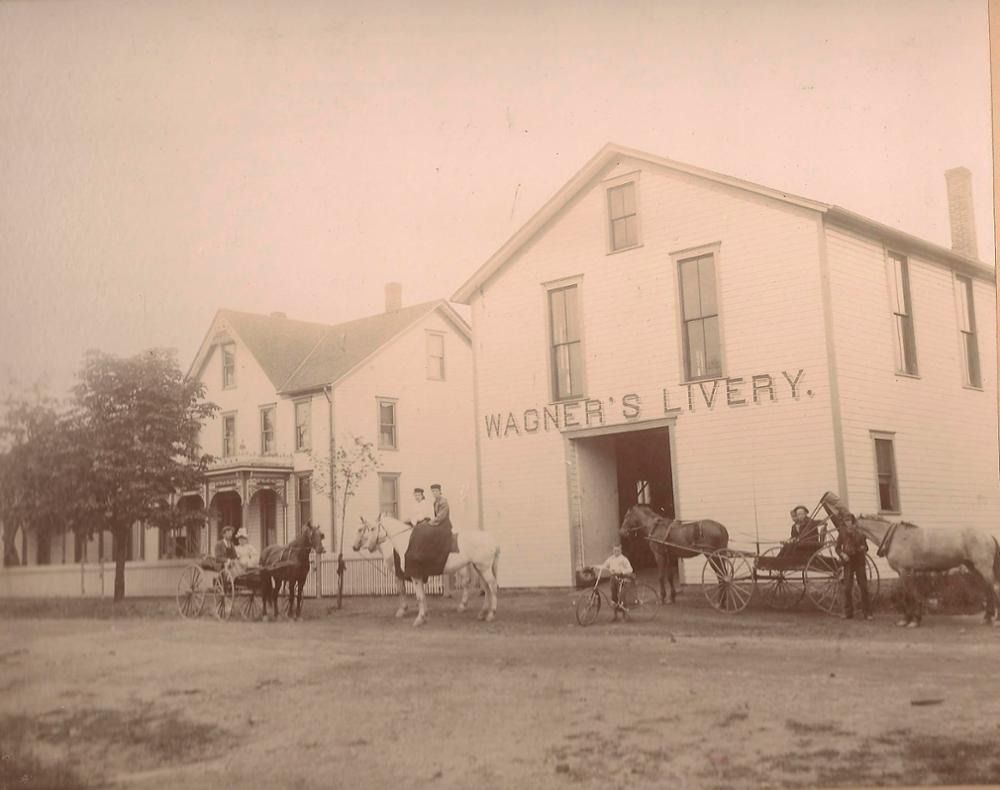Wagner's Livery stable with horses and carriages. People standing outside.