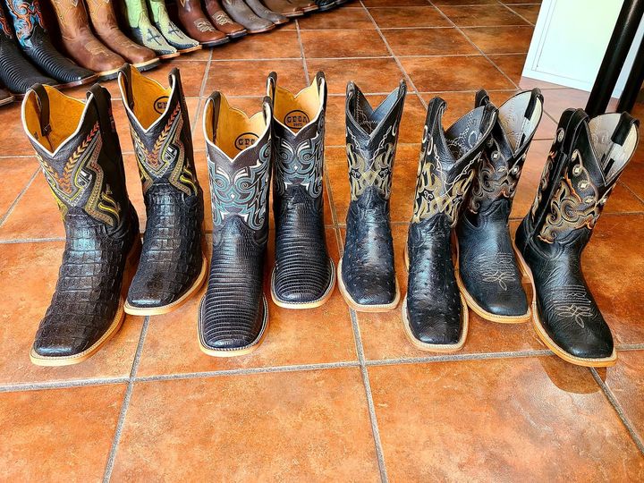 A row of cowboy boots are lined up on a tiled floor.