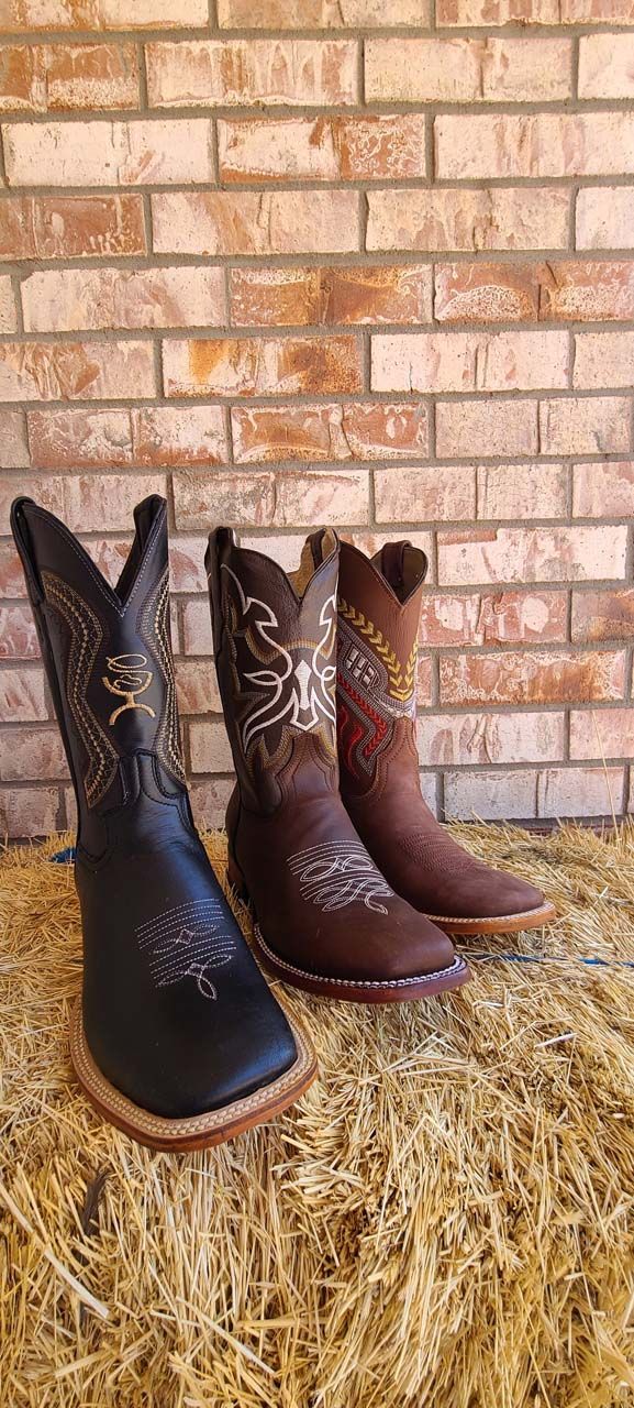 Two pairs of cowboy boots are sitting on a pile of hay in front of a brick wall.