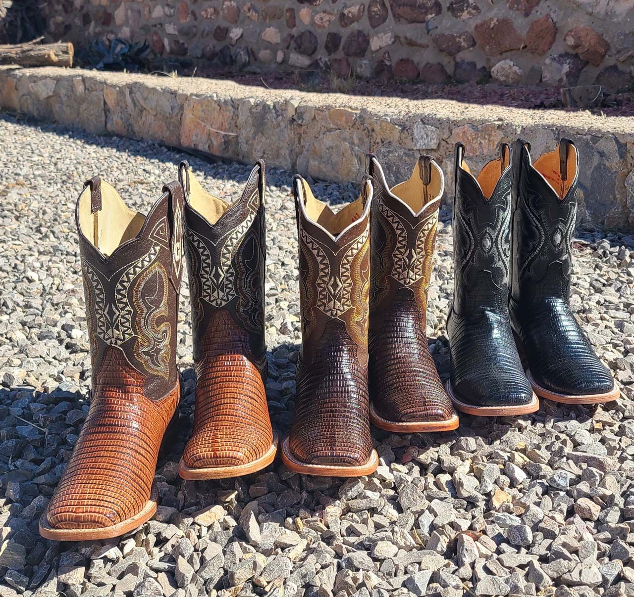 Four pairs of cowboy boots are lined up on gravel